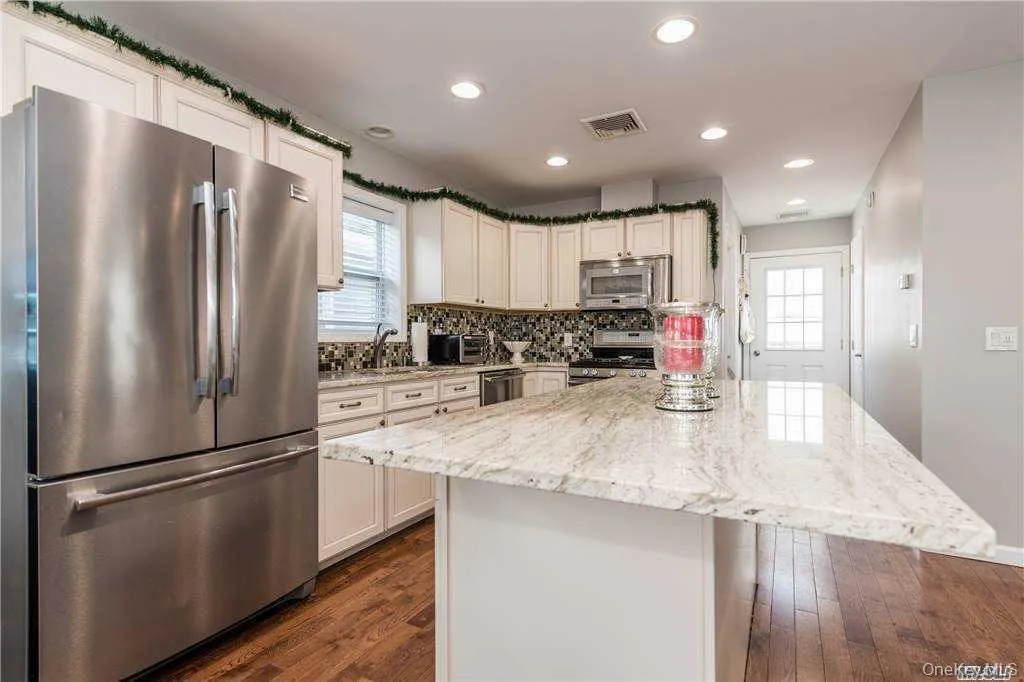 Kitchen featuring stainless steel appliances, light stone countertops, recessed lighting, backsplash, and a kitchen island Kitchen featuring stainless steel appliances, light stone countertops, recessed lighting, backsplash, and a kitchen island