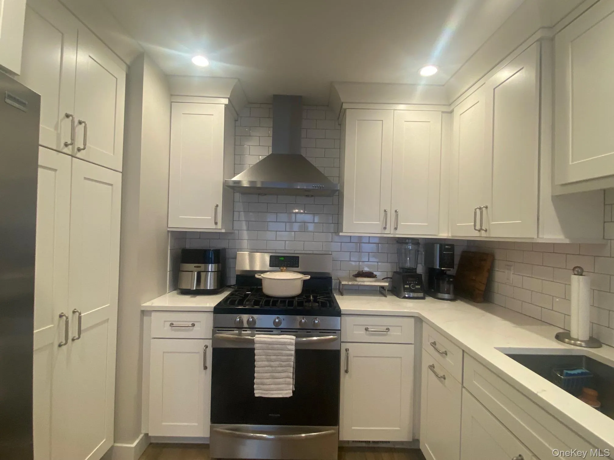 Kitchen featuring appliances with stainless steel finishes, wall chimney range hood, backsplash, white cabinets, and light stone countertops Kitchen featuring appliances with stainless steel finishes, wall chimney range hood, backsplash, white cabinets, and light stone countertops