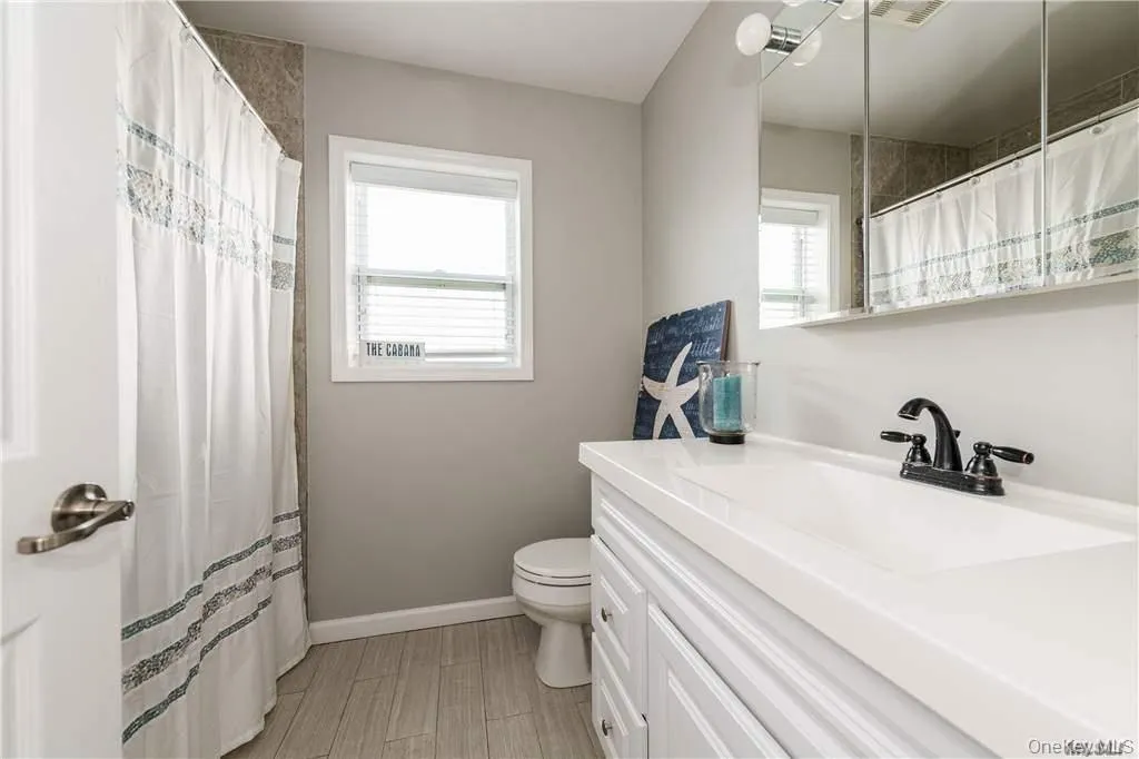 Full bath with a shower with shower curtain, vanity, and wood finish floors Full bath with a shower with shower curtain, vanity, and wood finish floors