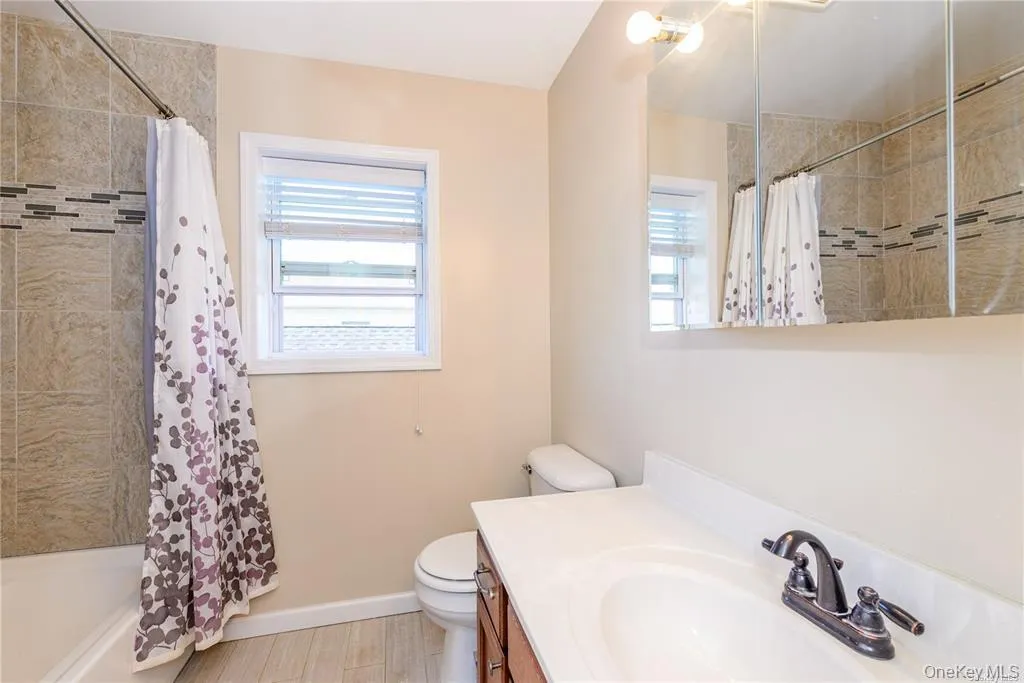 Bathroom featuring vanity, shower / bath combination with curtain, plenty of natural light, and light wood-type flooring Bathroom featuring vanity, shower / bath combination with curtain, plenty of natural light, and light wood-type flooring