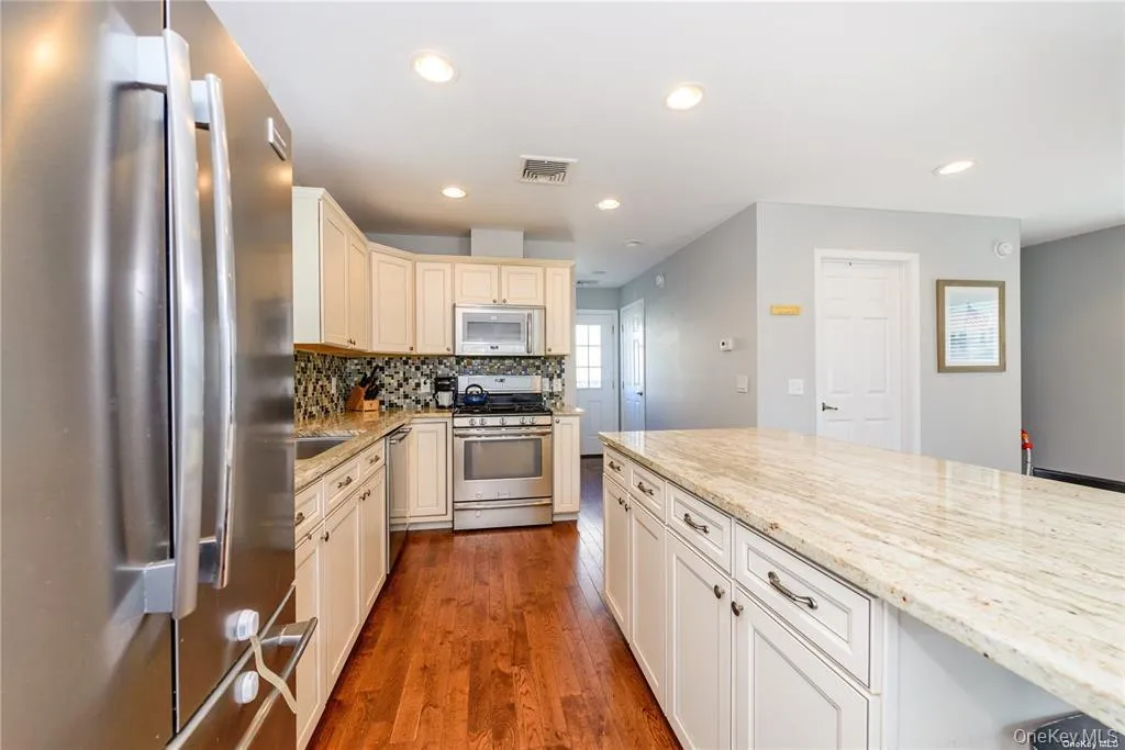 Kitchen featuring appliances with stainless steel finishes, light stone countertops, dark wood-style flooring, recessed lighting, and tasteful backsplash Kitchen featuring appliances with stainless steel finishes, light stone countertops, dark wood-style flooring, recessed lighting, and tasteful backsplash