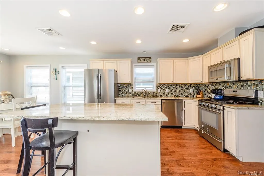 Kitchen featuring appliances with stainless steel finishes, light stone countertops, recessed lighting, cream cabinetry, and a kitchen island Kitchen featuring appliances with stainless steel finishes, light stone countertops, recessed lighting, cream cabinetry, and a kitchen island