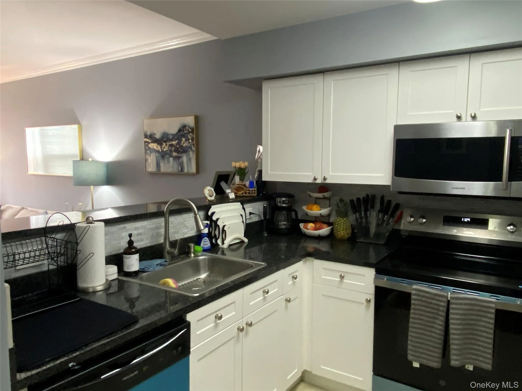 Kitchen featuring appliances with stainless steel finishes, white cabinetry, tasteful backsplash, open floor plan, and crown molding Kitchen featuring appliances with stainless steel finishes, white cabinetry, tasteful backsplash, open floor plan, and crown molding