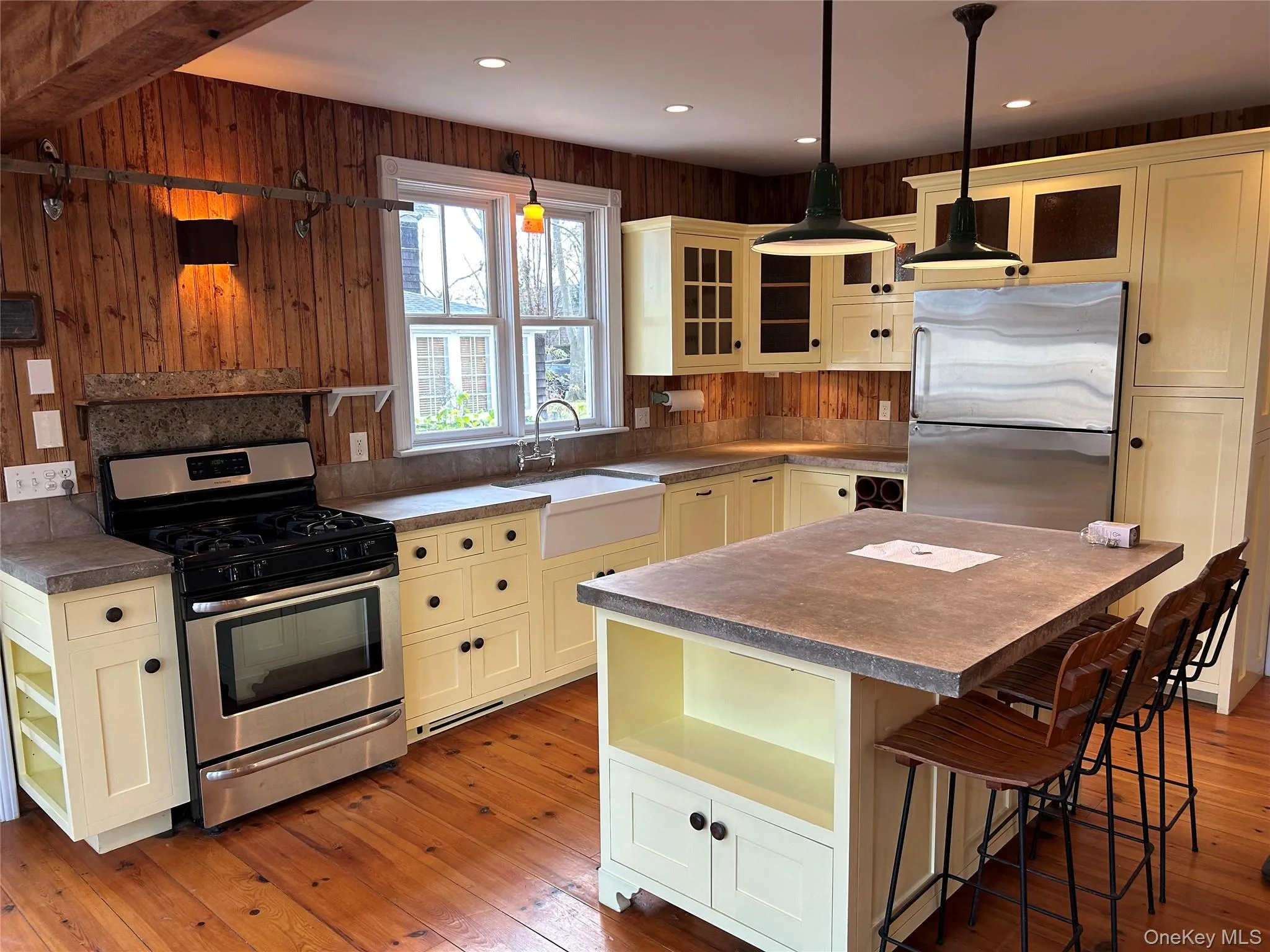Kitchen with stainless steel appliances, a breakfast bar area, light wood-style floors, cream cabinetry, and decorative light fixtures Kitchen with stainless steel appliances, a breakfast bar area, light wood-style floors, cream cabinetry, and decorative light fixtures