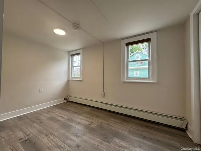 Empty room featuring a baseboard heating unit, wood finished floors, and a smoke detector Empty room featuring a baseboard heating unit, wood finished floors, and a smoke detector