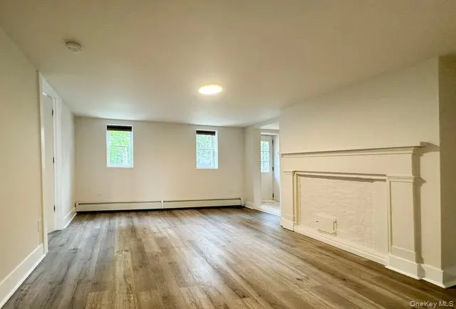 Unfurnished living room with wood finished floors and a baseboard heating unit Unfurnished living room with wood finished floors and a baseboard heating unit