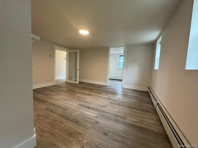 Empty room with baseboard heating, wood finished floors, and a baseboard radiator Empty room with baseboard heating, wood finished floors, and a baseboard radiator