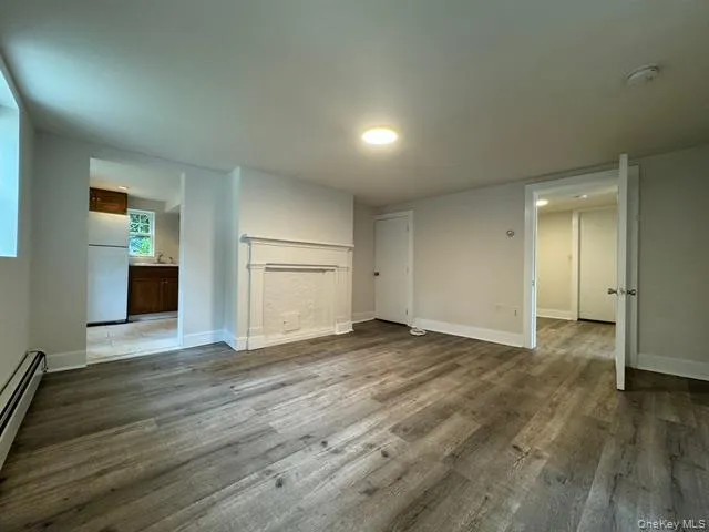 Unfurnished living room featuring dark wood-type flooring and a baseboard heating unit Unfurnished living room featuring dark wood-type flooring and a baseboard heating unit
