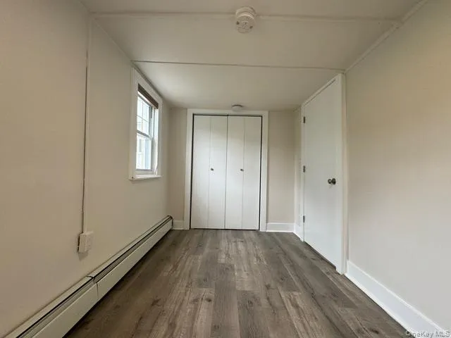 Unfurnished bedroom featuring a baseboard heating unit, dark wood-style flooring, and a closet Unfurnished bedroom featuring a baseboard heating unit, dark wood-style flooring, and a closet