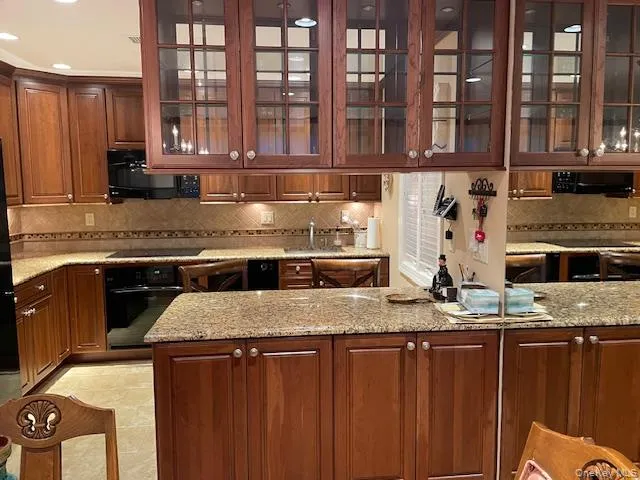 Kitchen with glass insert cabinets, backsplash, black appliances, light stone countertops, and recessed lighting Kitchen with glass insert cabinets, backsplash, black appliances, light stone countertops, and recessed lighting