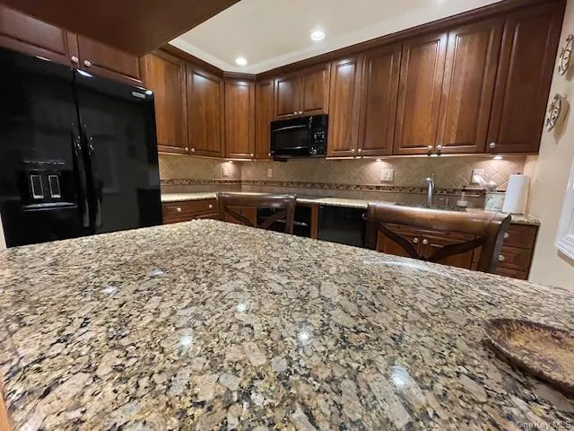 Kitchen with black appliances, light stone counters, and tasteful backsplash Kitchen with black appliances, light stone counters, and tasteful backsplash