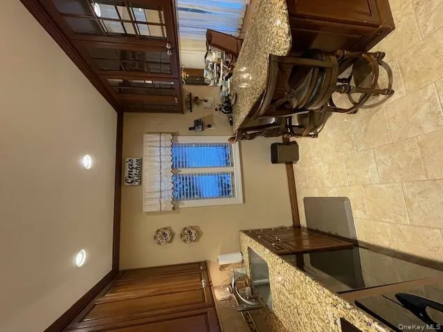 Kitchen featuring light stone countertops, a breakfast bar area, dark brown cabinetry, crown molding, and glass insert cabinets Kitchen featuring light stone countertops, a breakfast bar area, dark brown cabinetry, crown molding, and glass insert cabinets