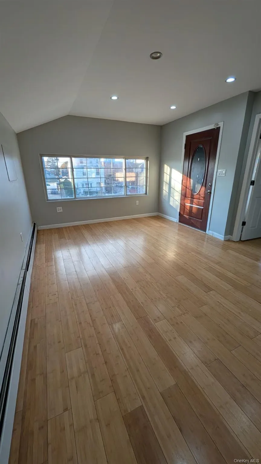Unfurnished living room with a baseboard heating unit, light wood-type flooring, recessed lighting, and lofted ceiling Unfurnished living room with a baseboard heating unit, light wood-type flooring, recessed lighting, and lofted ceiling