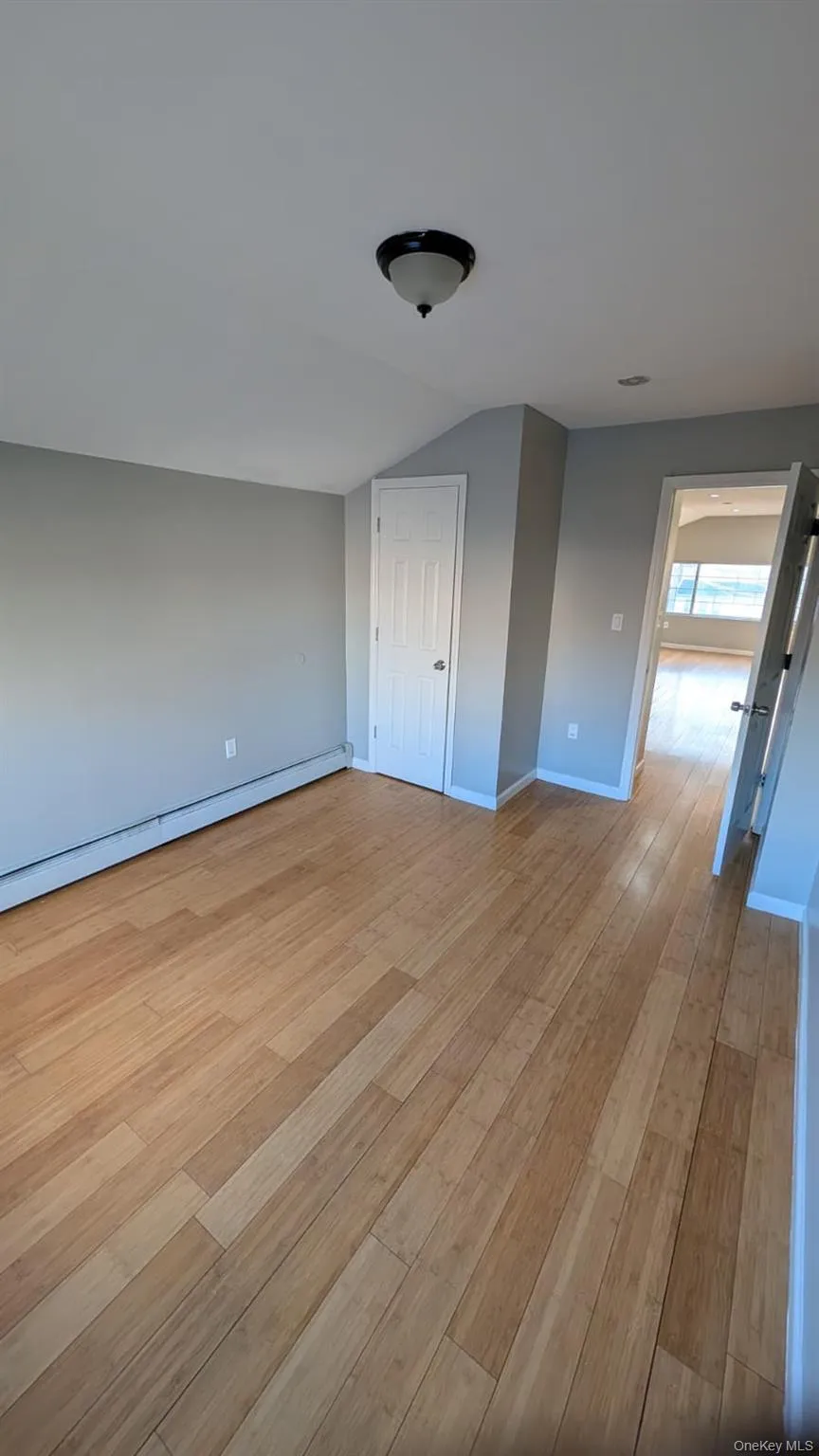 Unfurnished bedroom featuring a baseboard radiator, vaulted ceiling, and light wood finished floors Unfurnished bedroom featuring a baseboard radiator, vaulted ceiling, and light wood finished floors