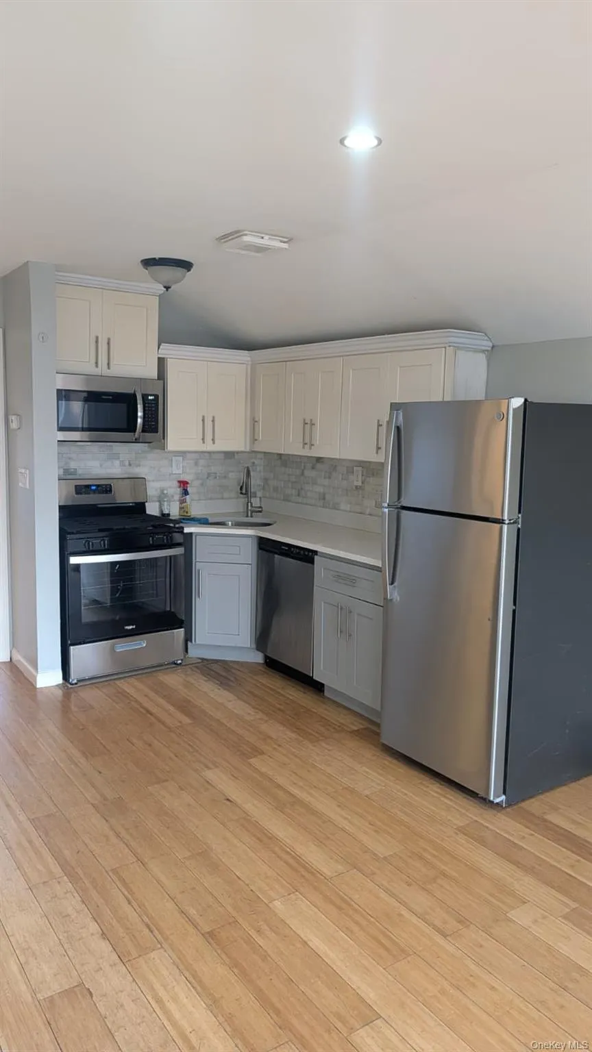 Kitchen with stainless steel appliances, light countertops, white cabinets, light wood-style floors, and tasteful backsplash Kitchen with stainless steel appliances, light countertops, white cabinets, light wood-style floors, and tasteful backsplash