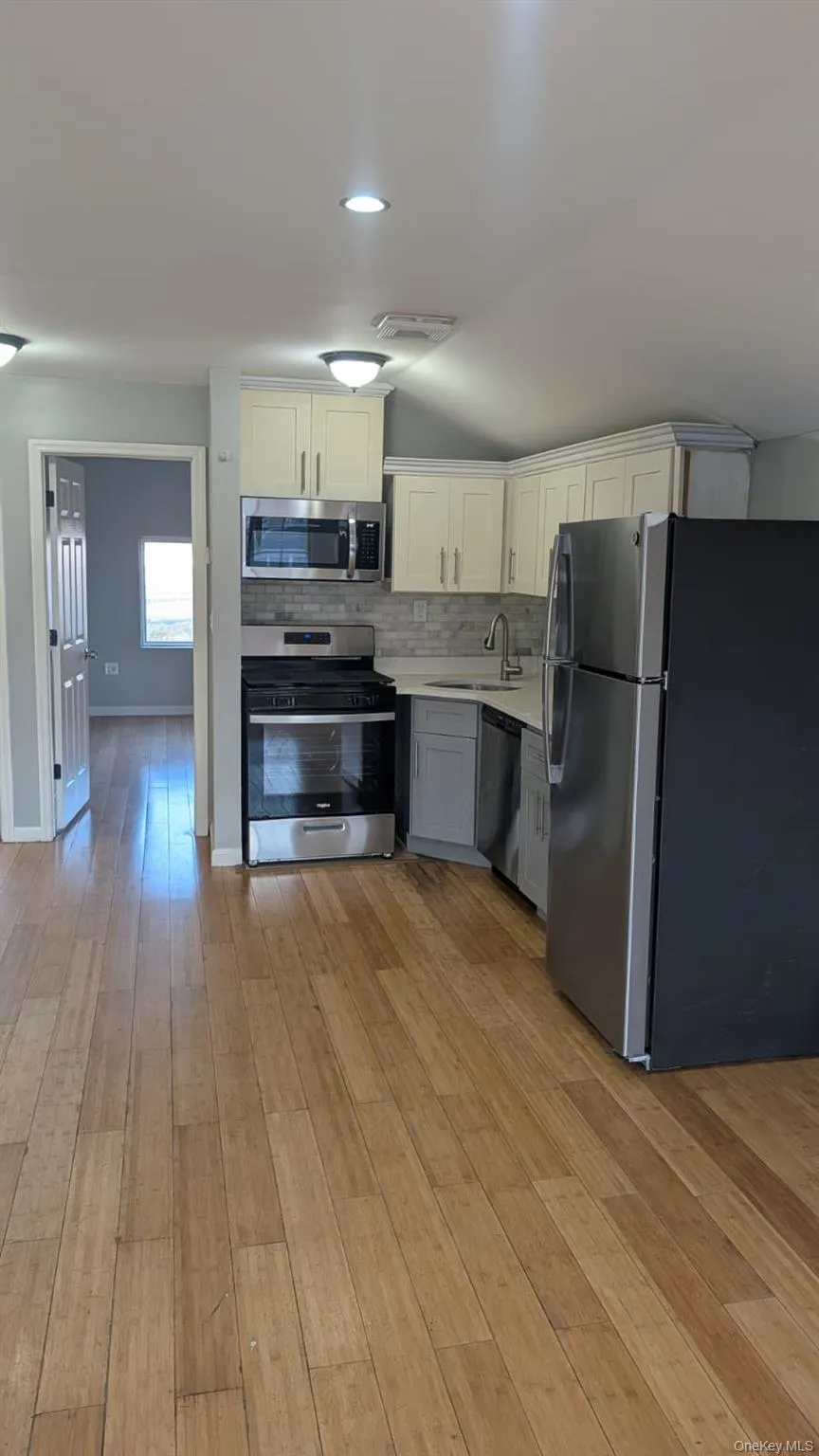 Kitchen with stainless steel appliances, gray cabinets, white cabinetry, decorative backsplash, and light wood finished floors Kitchen with stainless steel appliances, gray cabinets, white cabinetry, decorative backsplash, and light wood finished floors