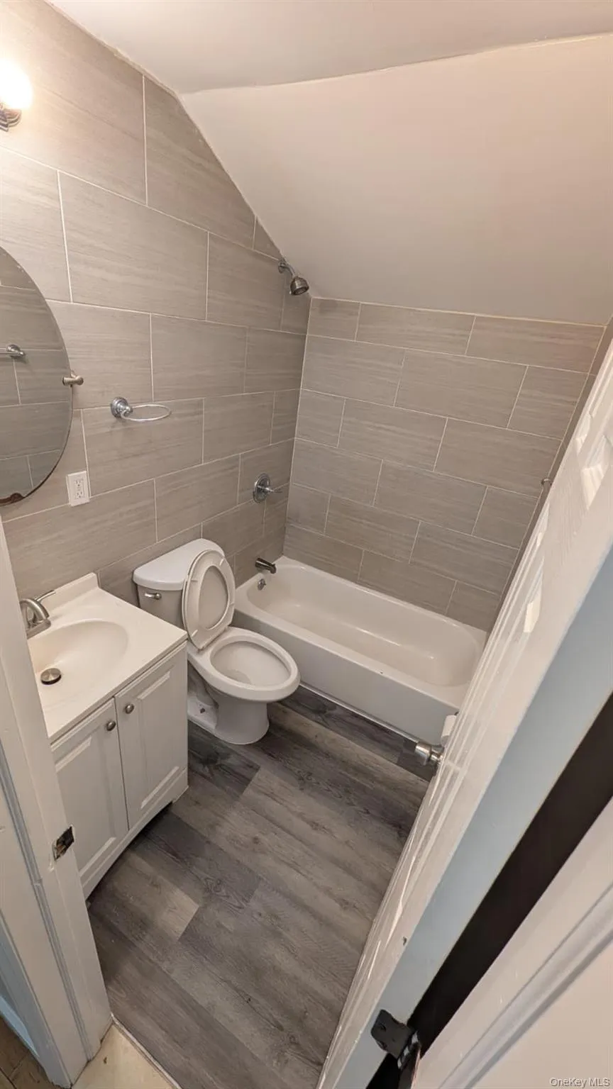 Bathroom featuring vanity, vaulted ceiling, shower / washtub combination, tile walls, and light wood-style flooring Bathroom featuring vanity, vaulted ceiling, shower / washtub combination, tile walls, and light wood-style flooring
