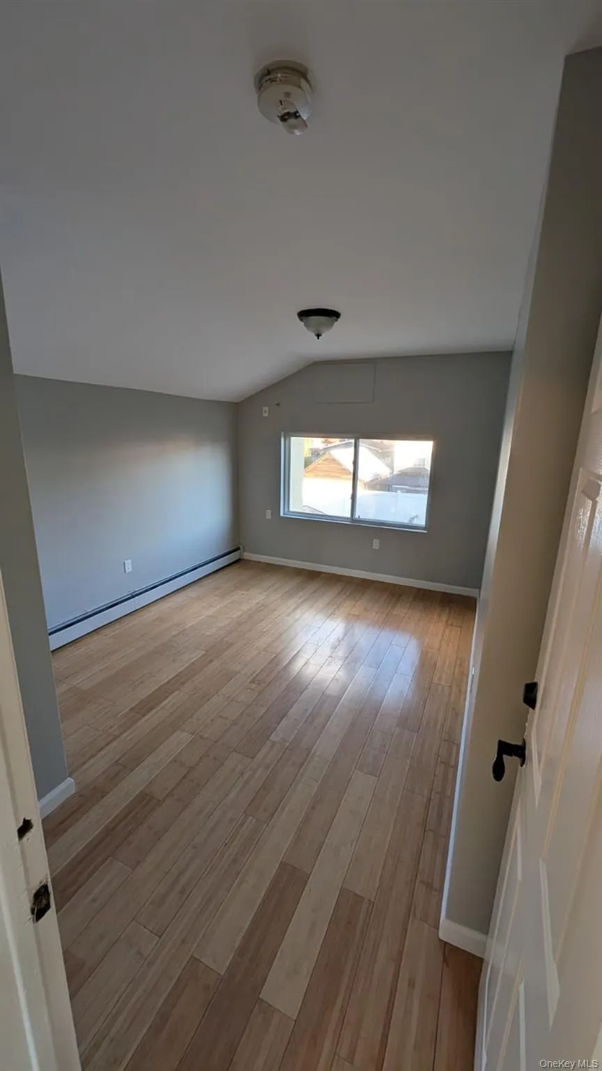 Empty room featuring baseboard heating, lofted ceiling, and light wood-style floors Empty room featuring baseboard heating, lofted ceiling, and light wood-style floors
