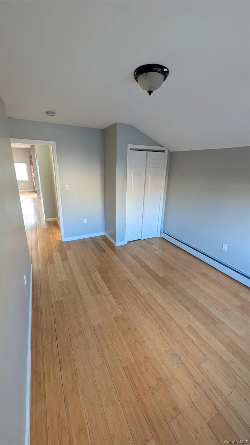 Unfurnished bedroom featuring a baseboard heating unit, a closet, light wood-style flooring, and vaulted ceiling Unfurnished bedroom featuring a baseboard heating unit, a closet, light wood-style flooring, and vaulted ceiling