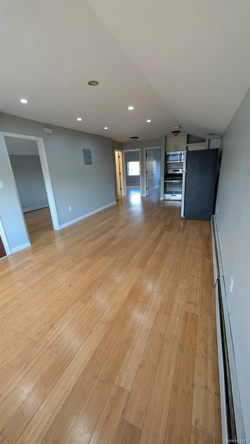 Unfurnished living room with recessed lighting, light wood-style floors, lofted ceiling, and a baseboard radiator Unfurnished living room with recessed lighting, light wood-style floors, lofted ceiling, and a baseboard radiator
