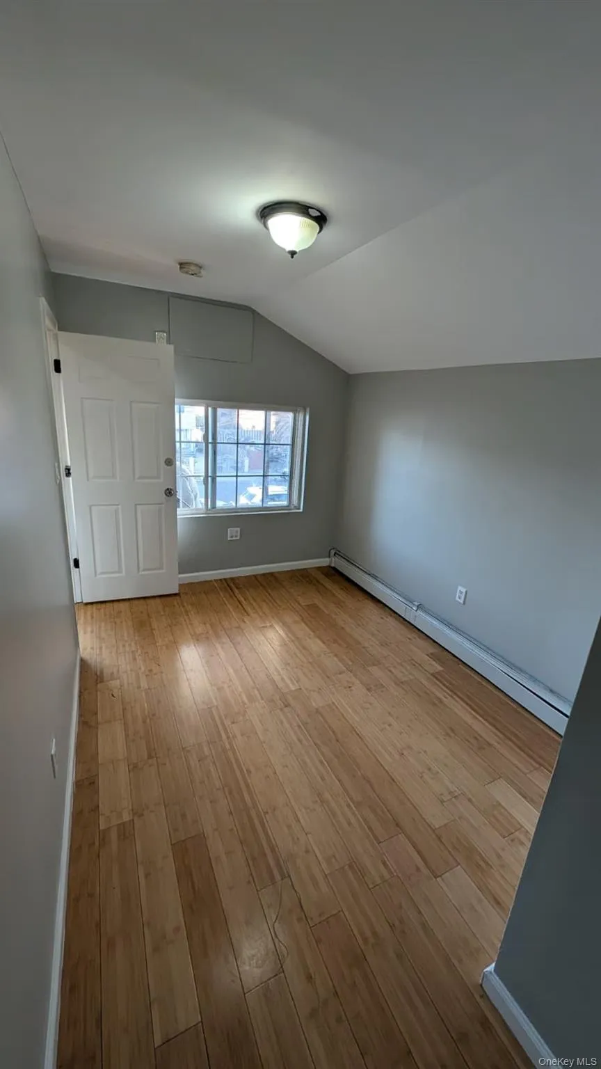 Unfurnished room with baseboard heating, lofted ceiling, and light wood-style flooring Unfurnished room with baseboard heating, lofted ceiling, and light wood-style flooring