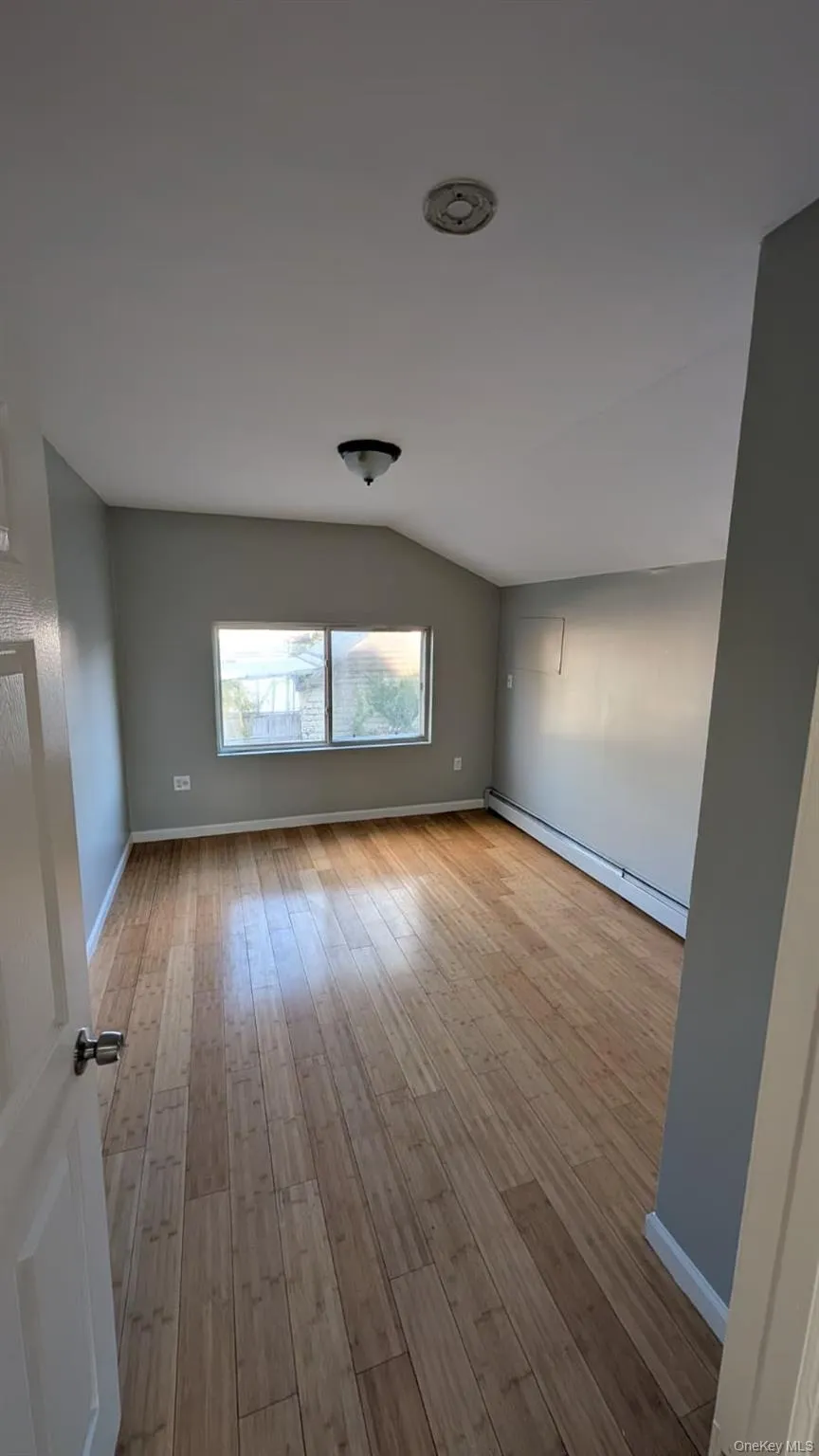 Unfurnished room with lofted ceiling, light wood finished floors, and baseboard heating Unfurnished room with lofted ceiling, light wood finished floors, and baseboard heating