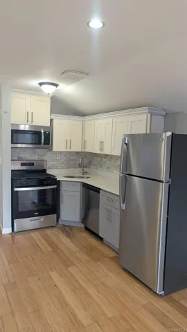 Kitchen featuring appliances with stainless steel finishes, white cabinets, vaulted ceiling, gray cabinetry, and backsplash