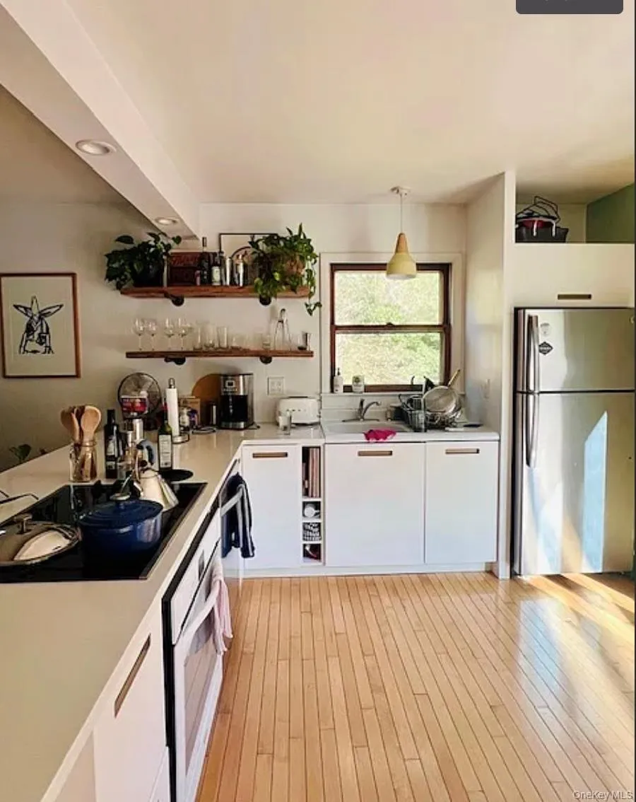 Kitchen featuring stainless steel appliances, light countertops, open shelves, white cabinets, and pendant lighting Kitchen featuring stainless steel appliances, light countertops, open shelves, white cabinets, and pendant lighting