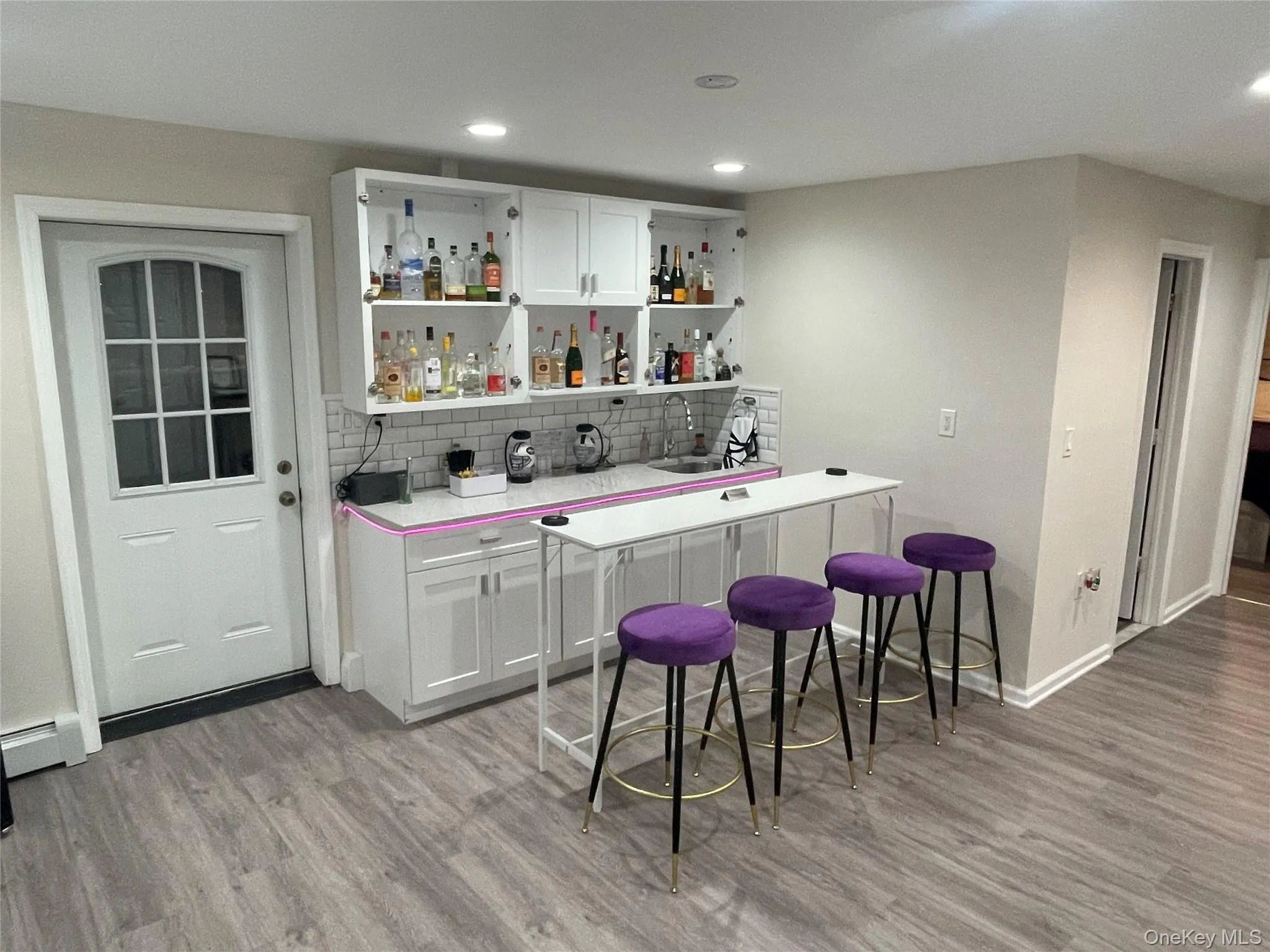 Indoor wet bar with light countertops, white cabinetry, a baseboard heating unit, open shelves, and light wood-style flooring Indoor wet bar with light countertops, white cabinetry, a baseboard heating unit, open shelves, and light wood-style flooring