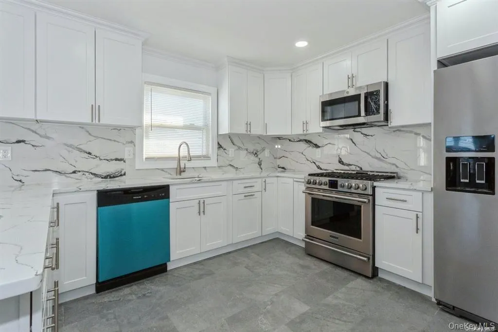 Kitchen featuring appliances with stainless steel finishes, white cabinets, light stone countertops, tasteful backsplash, and ornamental molding Kitchen featuring appliances with stainless steel finishes, white cabinets, light stone countertops, tasteful backsplash, and ornamental molding