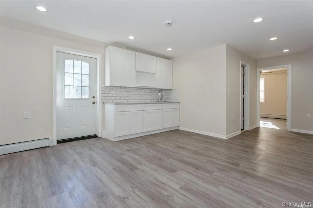 Kitchen featuring white cabinetry, light wood-style floors, light countertops, decorative backsplash Kitchen featuring white cabinetry, light wood-style floors, light countertops, decorative backsplash