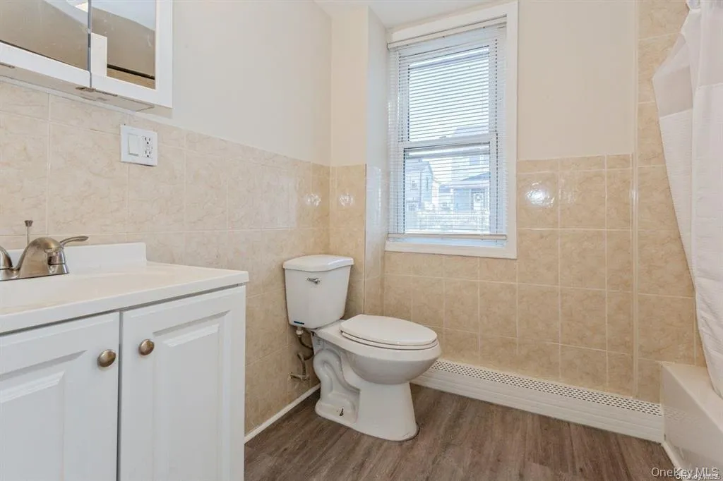 Full bathroom with vanity, tile walls, baseboard heating, wood finished floors, and shower / tub combo with curtain Full bathroom with vanity, tile walls, baseboard heating, wood finished floors, and shower / tub combo with curtain