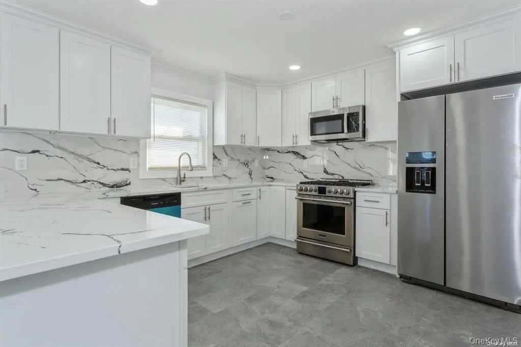 Kitchen with stainless steel appliances, white cabinets, light stone countertops, ornamental molding, and backsplash Kitchen with stainless steel appliances, white cabinets, light stone countertops, ornamental molding, and backsplash