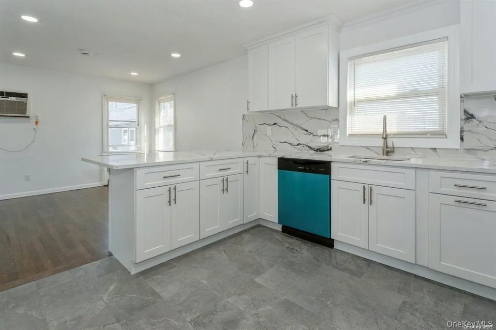 Kitchen with white cabinets, dishwashing machine, a peninsula, light stone countertops, and tasteful backsplash Kitchen with white cabinets, dishwashing machine, a peninsula, light stone countertops, and tasteful backsplash