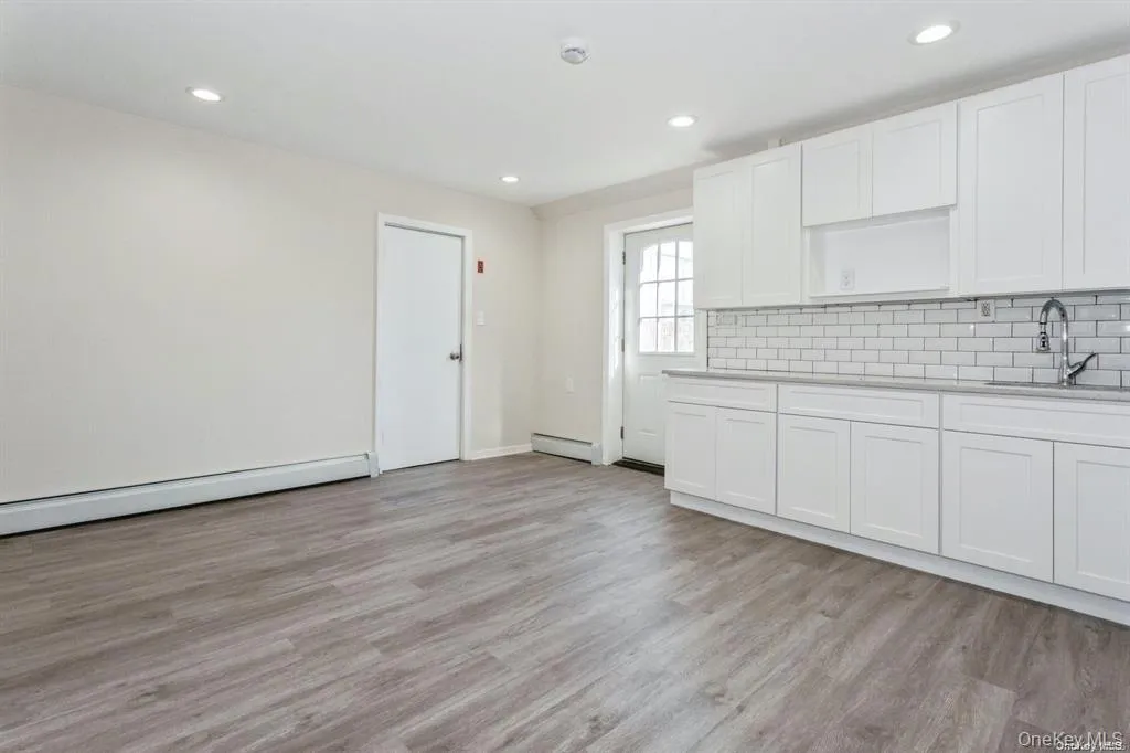 Kitchen with white cabinetry, light wood-style flooring, decorative backsplash, light stone counters Kitchen with white cabinetry, light wood-style flooring, decorative backsplash, light stone counters