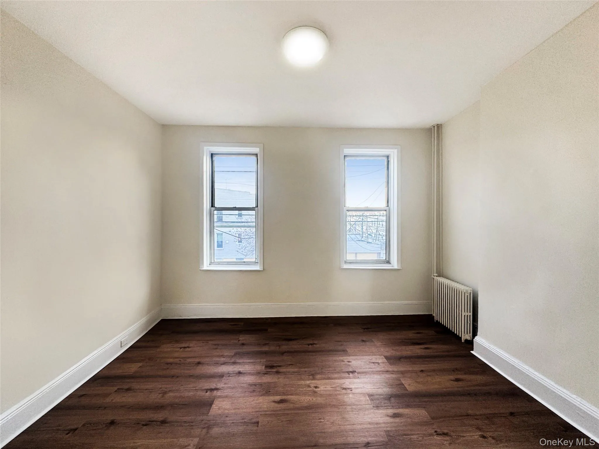 Spare room featuring dark wood-style flooring and radiator heating unit Spare room featuring dark wood-style flooring and radiator heating unit