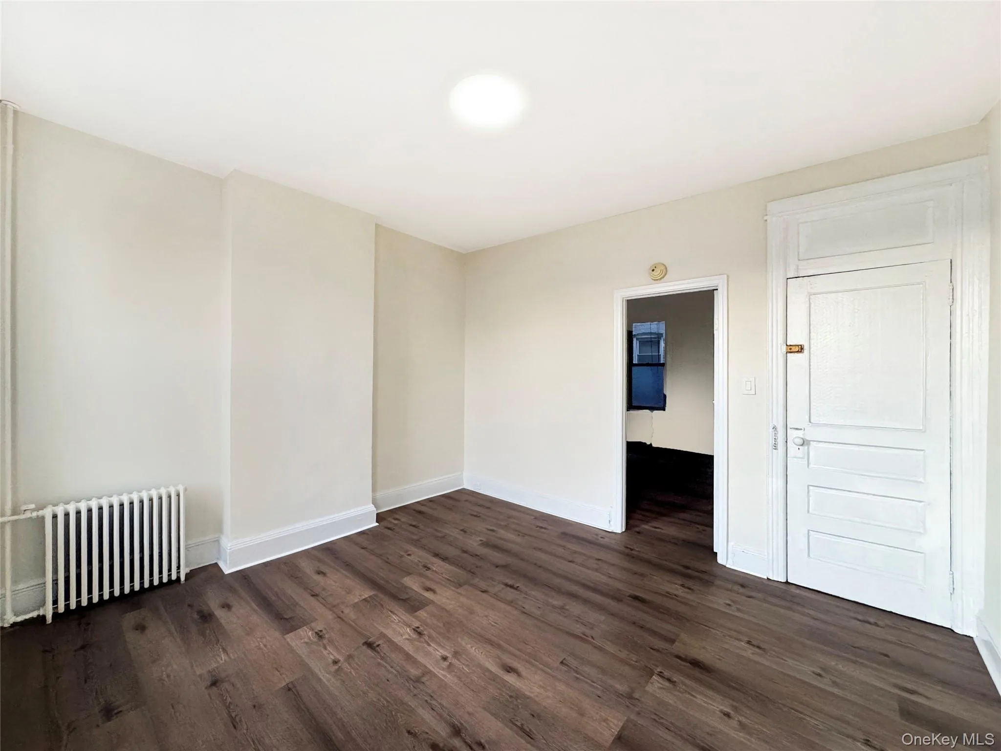 Unfurnished room featuring radiator heating unit and dark wood finished floors Unfurnished room featuring radiator heating unit and dark wood finished floors