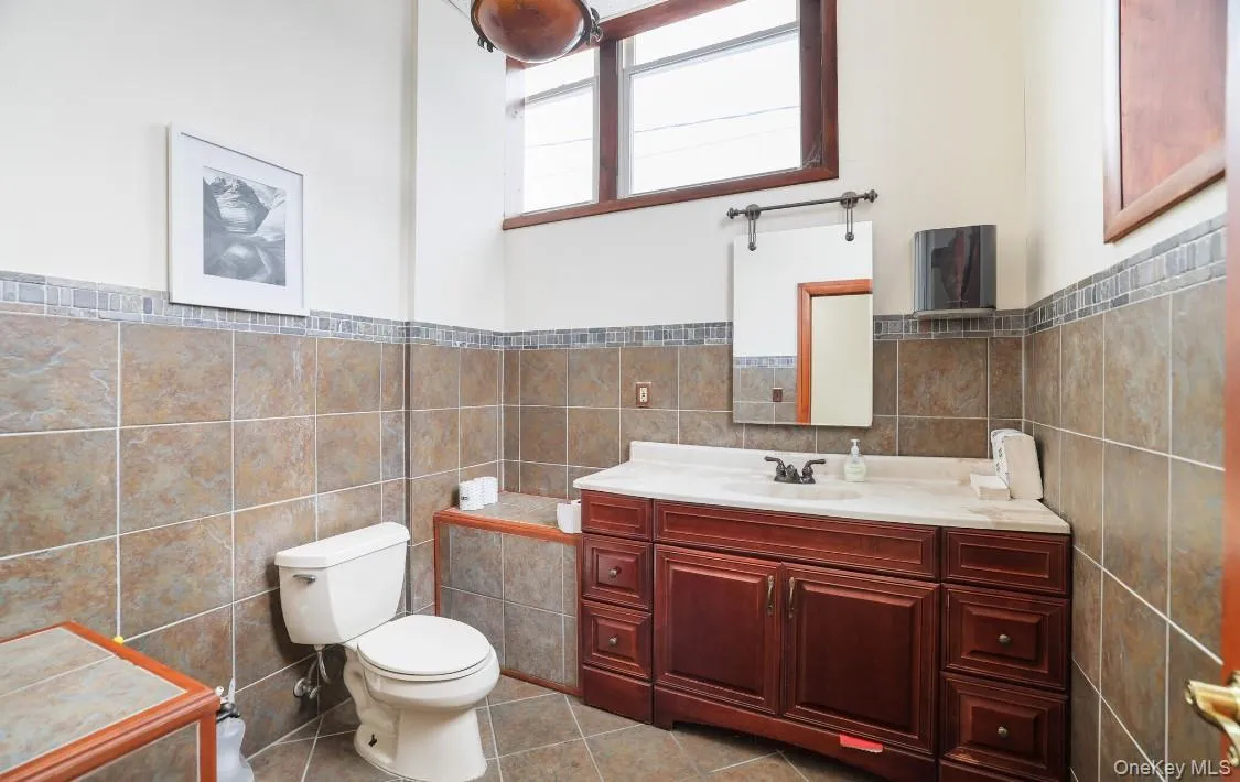 Half bathroom with tile patterned flooring, toilet, vanity, wainscoting, and tile walls Half bathroom with tile patterned flooring, toilet, vanity, wainscoting, and tile walls