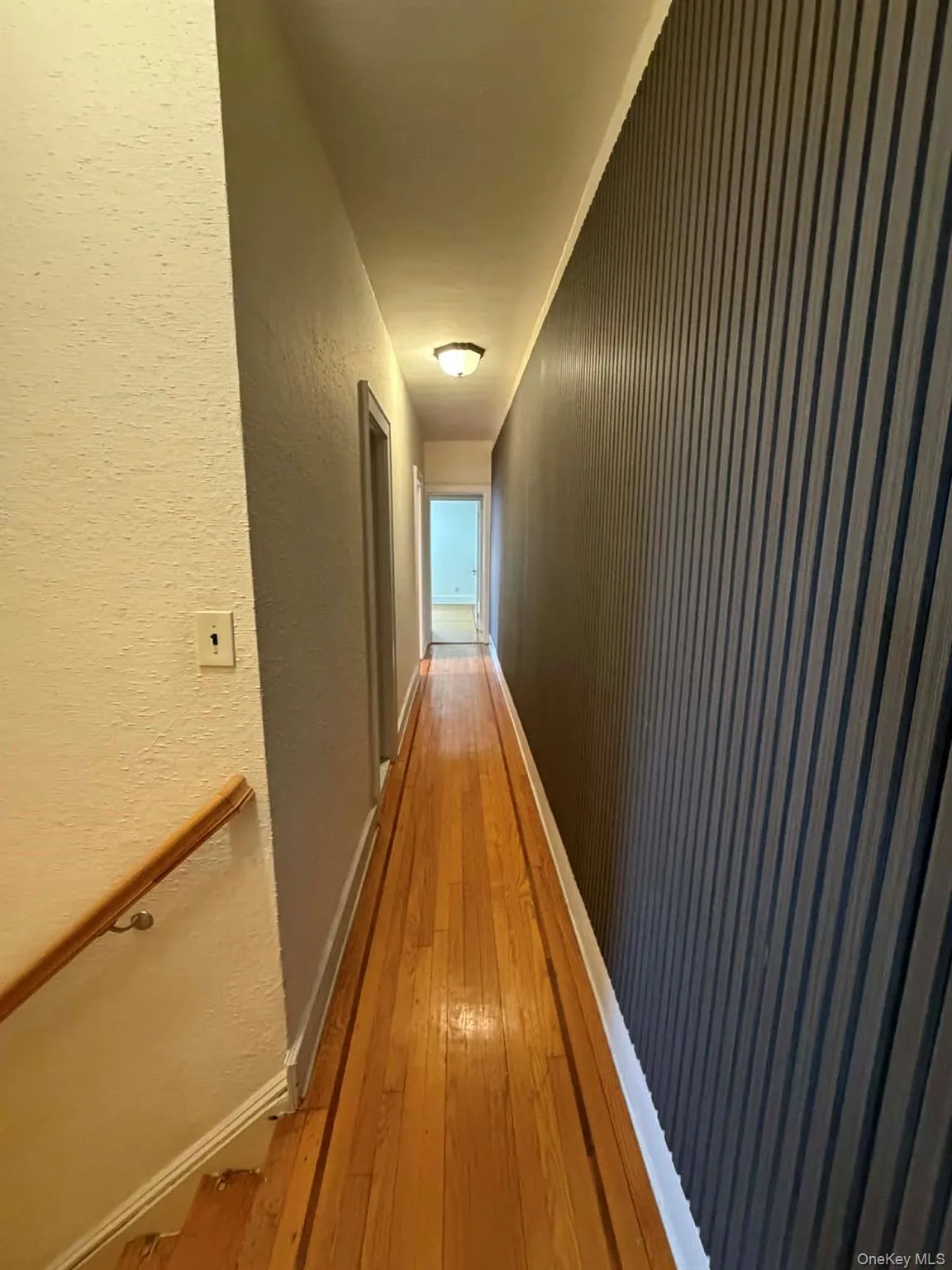 Hall featuring a textured wall, light wood-type flooring, and an upstairs landing Hall featuring a textured wall, light wood-type flooring, and an upstairs landing