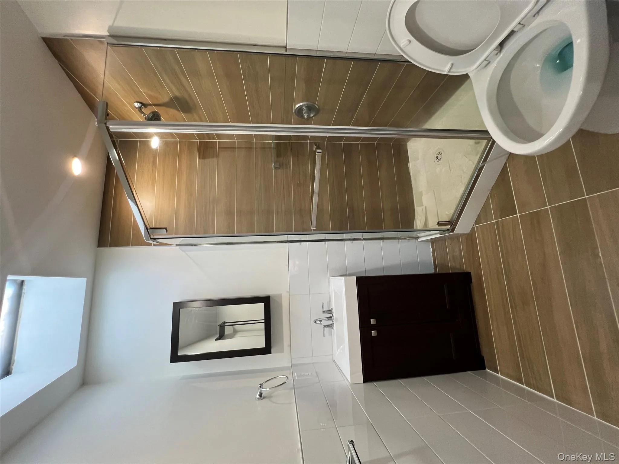 Full bathroom featuring tile walls, vanity, a shower stall, wainscoting, and dark tile patterned flooring Full bathroom featuring tile walls, vanity, a shower stall, wainscoting, and dark tile patterned flooring