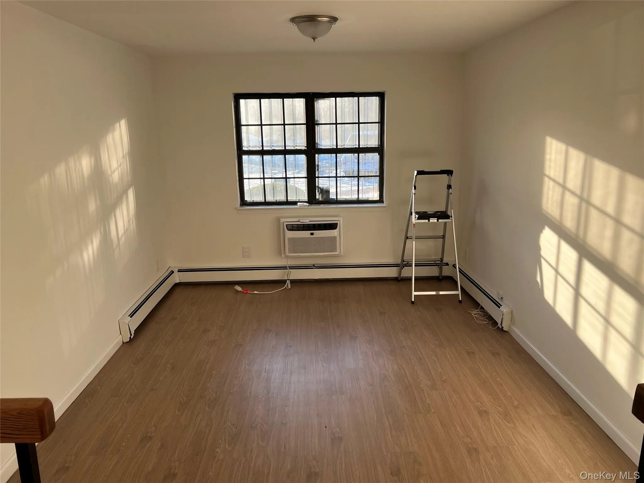Spare room featuring dark wood finished floors, baseboard heating, and a wall mounted air conditioner Spare room featuring dark wood finished floors, baseboard heating, and a wall mounted air conditioner