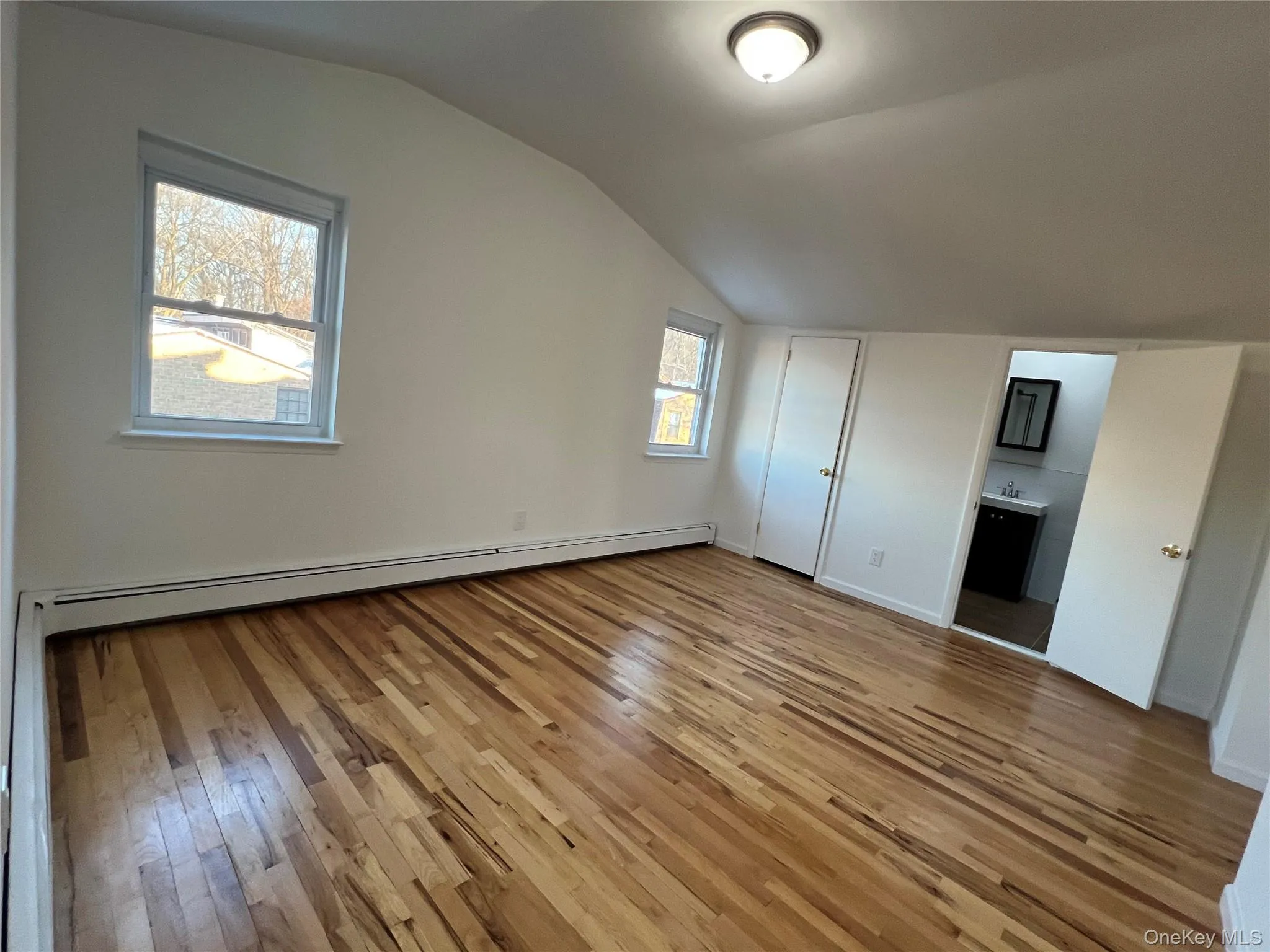 Unfurnished bedroom with light wood-style flooring, vaulted ceiling, a baseboard heating unit, and ensuite bath Unfurnished bedroom with light wood-style flooring, vaulted ceiling, a baseboard heating unit, and ensuite bath