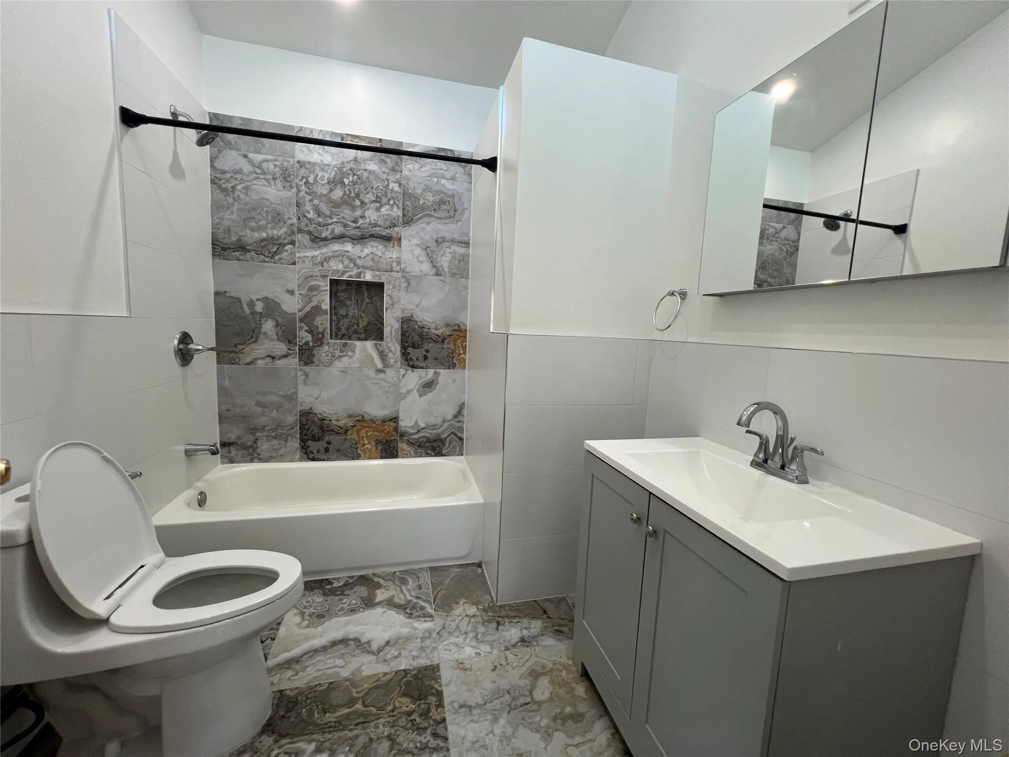 Full bath featuring tile walls, vanity, bathtub / shower combination, and light marble finish floors Full bath featuring tile walls, vanity, bathtub / shower combination, and light marble finish floors