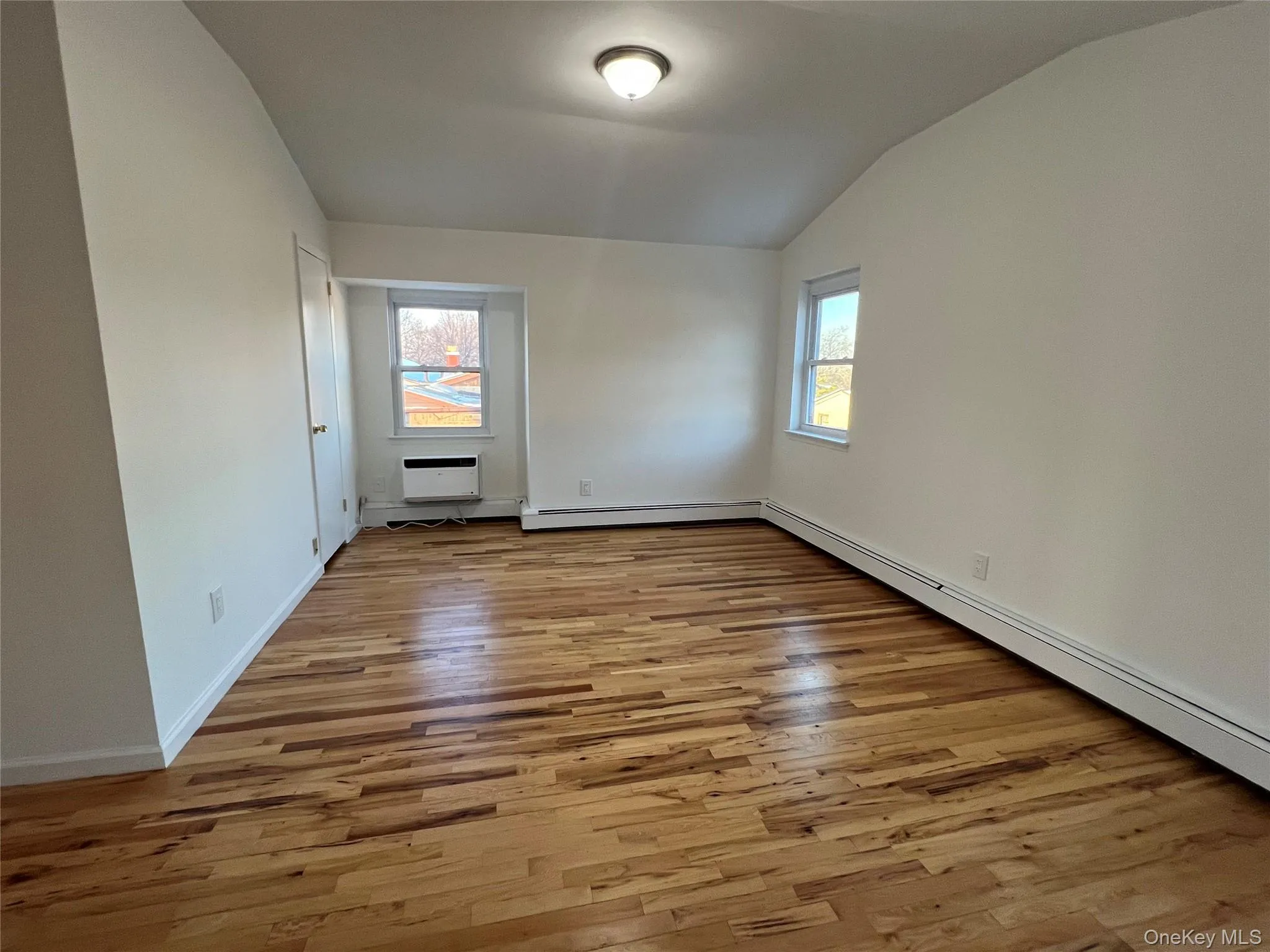 Unfurnished room with light wood finished floors, a baseboard heating unit, healthy amount of natural light, and vaulted ceiling Unfurnished room with light wood finished floors, a baseboard heating unit, healthy amount of natural light, and vaulted ceiling