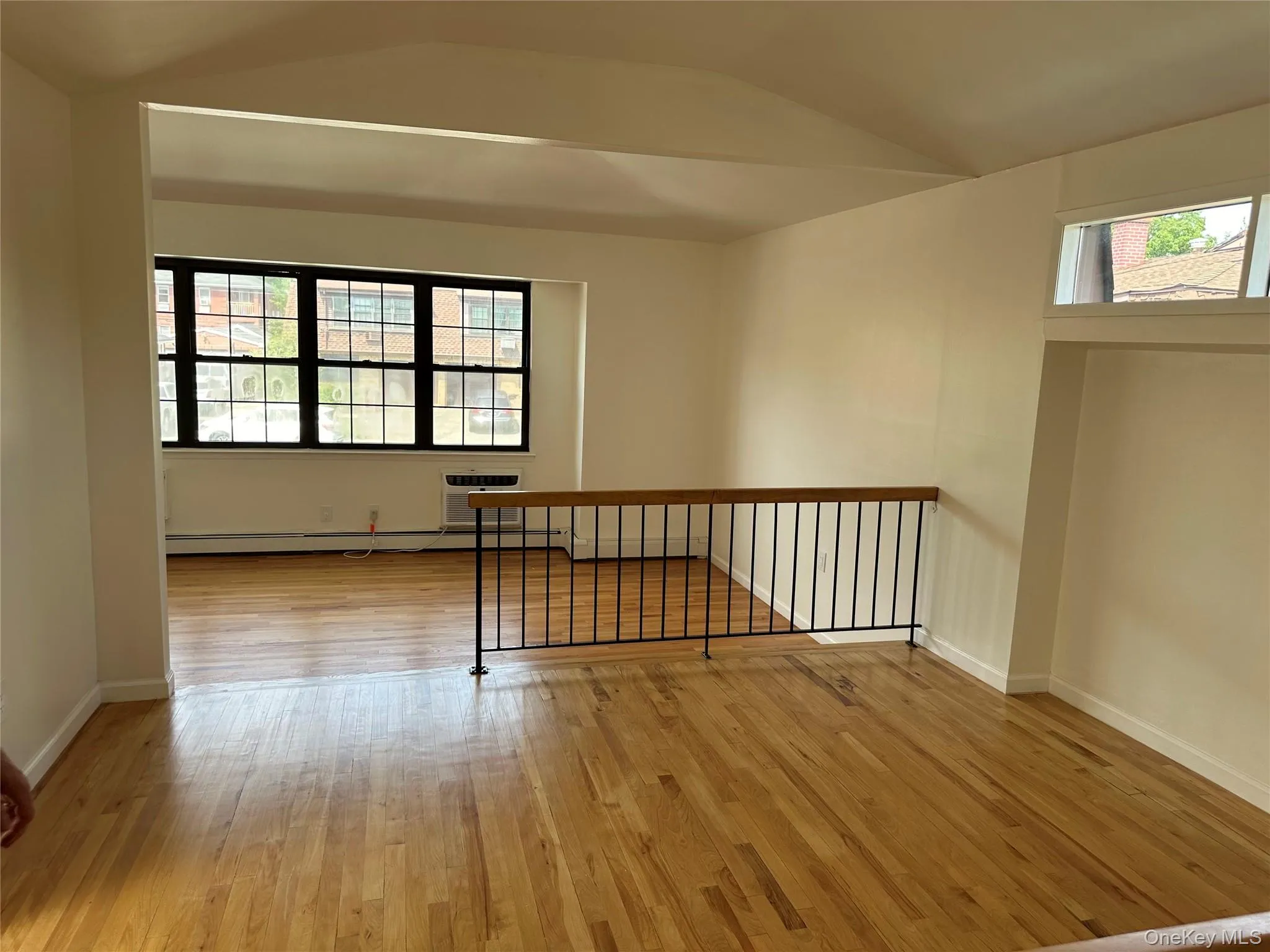 Spare room featuring light wood-style floors, vaulted ceiling, a wall mounted AC, and a baseboard heating unit Spare room featuring light wood-style floors, vaulted ceiling, a wall mounted AC, and a baseboard heating unit