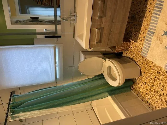 Full bathroom with toilet, tile walls, vanity, shower / bath combo with shower curtain, and backsplash Full bathroom with toilet, tile walls, vanity, shower / bath combo with shower curtain, and backsplash