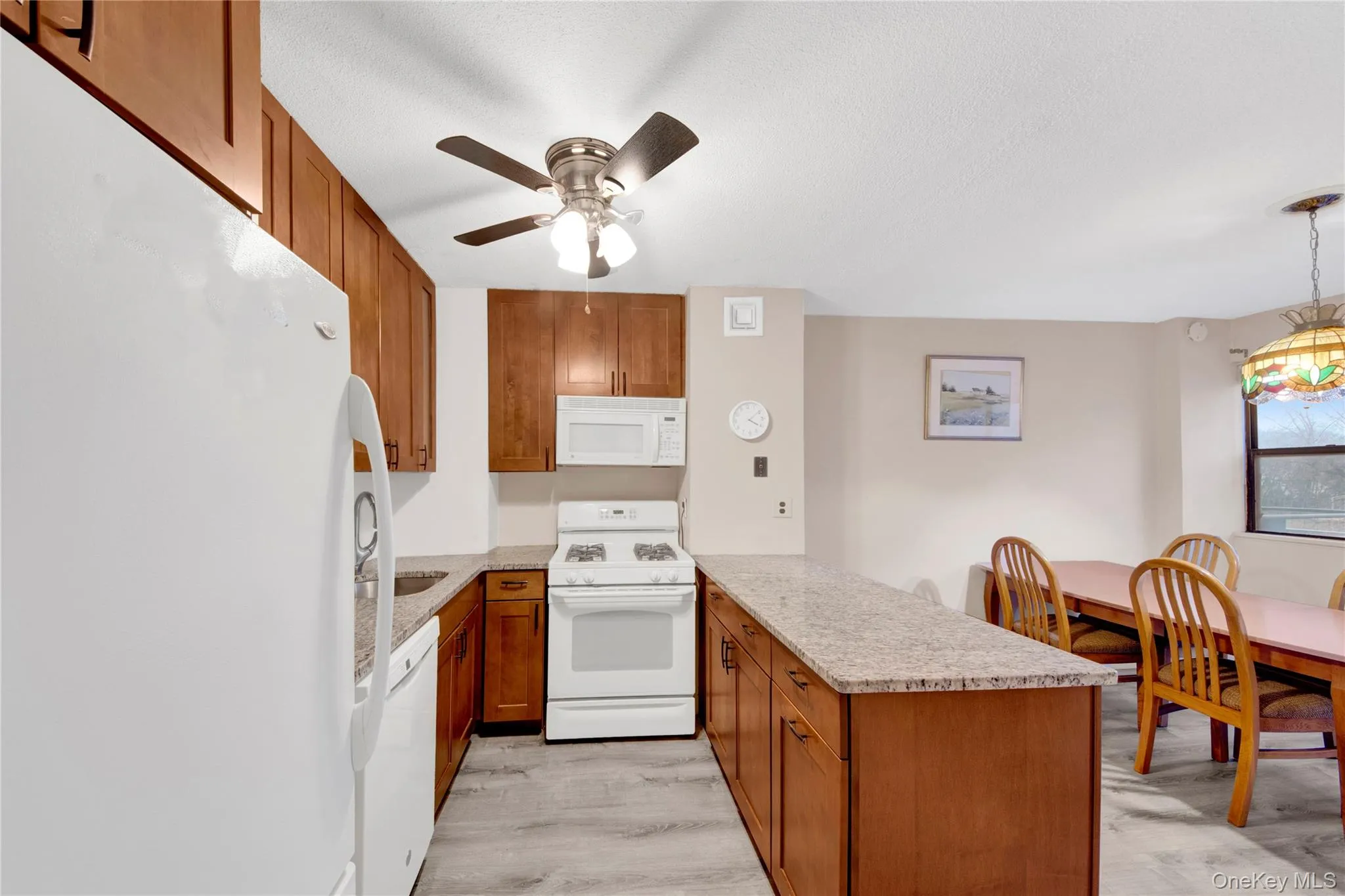 Kitchen with brown cabinets, white appliances, a peninsula, and light stone countertops Kitchen with brown cabinets, white appliances, a peninsula, and light stone countertops