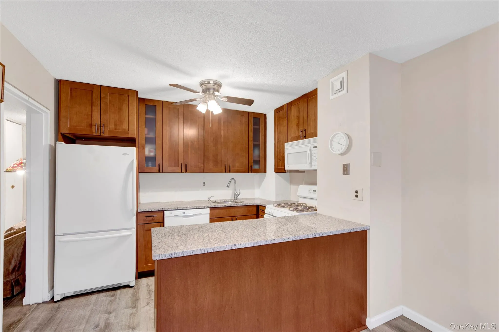 Kitchen with white appliances, brown cabinets, glass insert cabinets, light wood finished floors, and a ceiling fan Kitchen with white appliances, brown cabinets, glass insert cabinets, light wood finished floors, and a ceiling fan