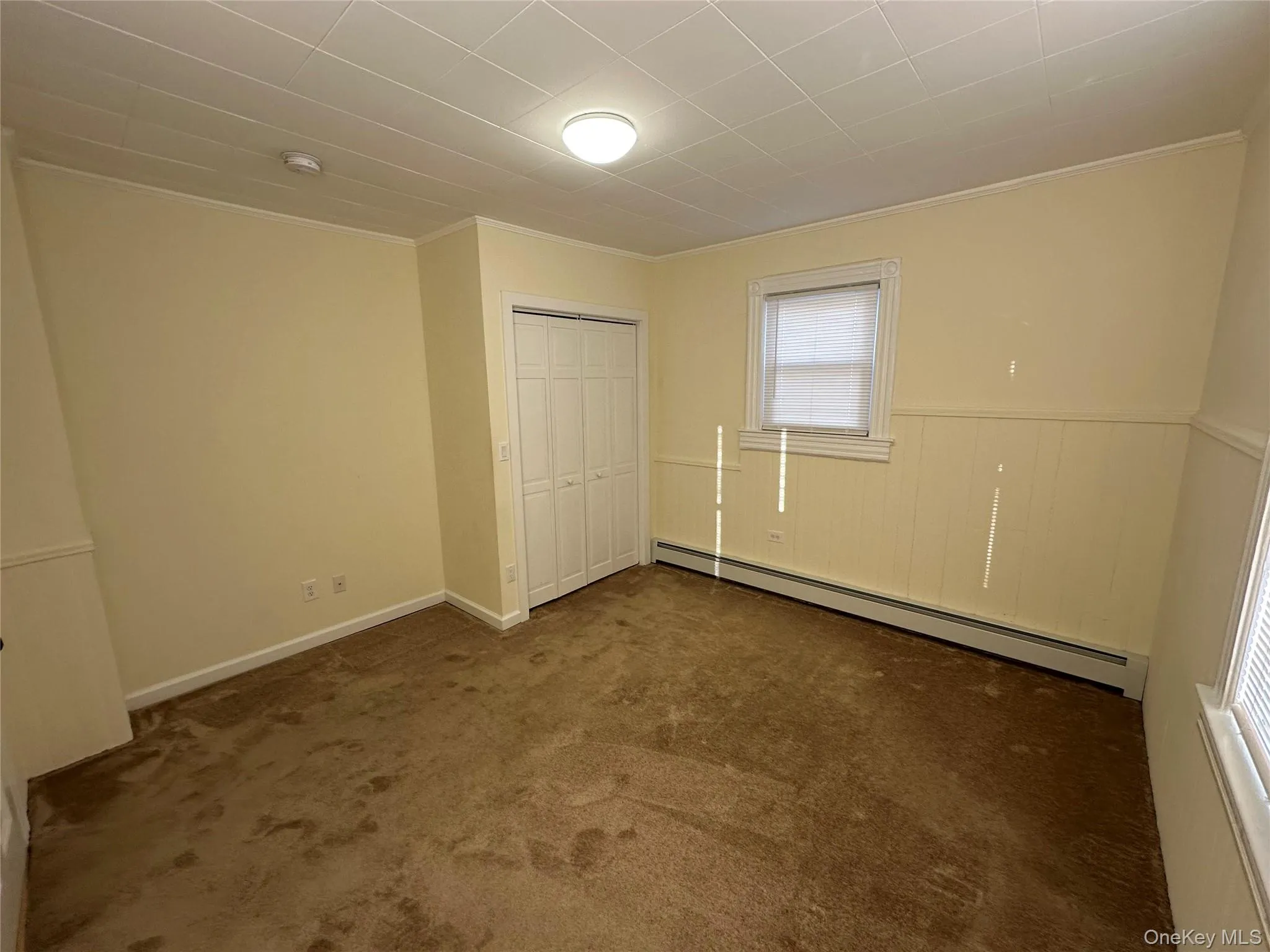 bedroom with baseboard heating, a closet, dark carpet, and crown molding bedroom with baseboard heating, a closet, dark carpet, and crown molding