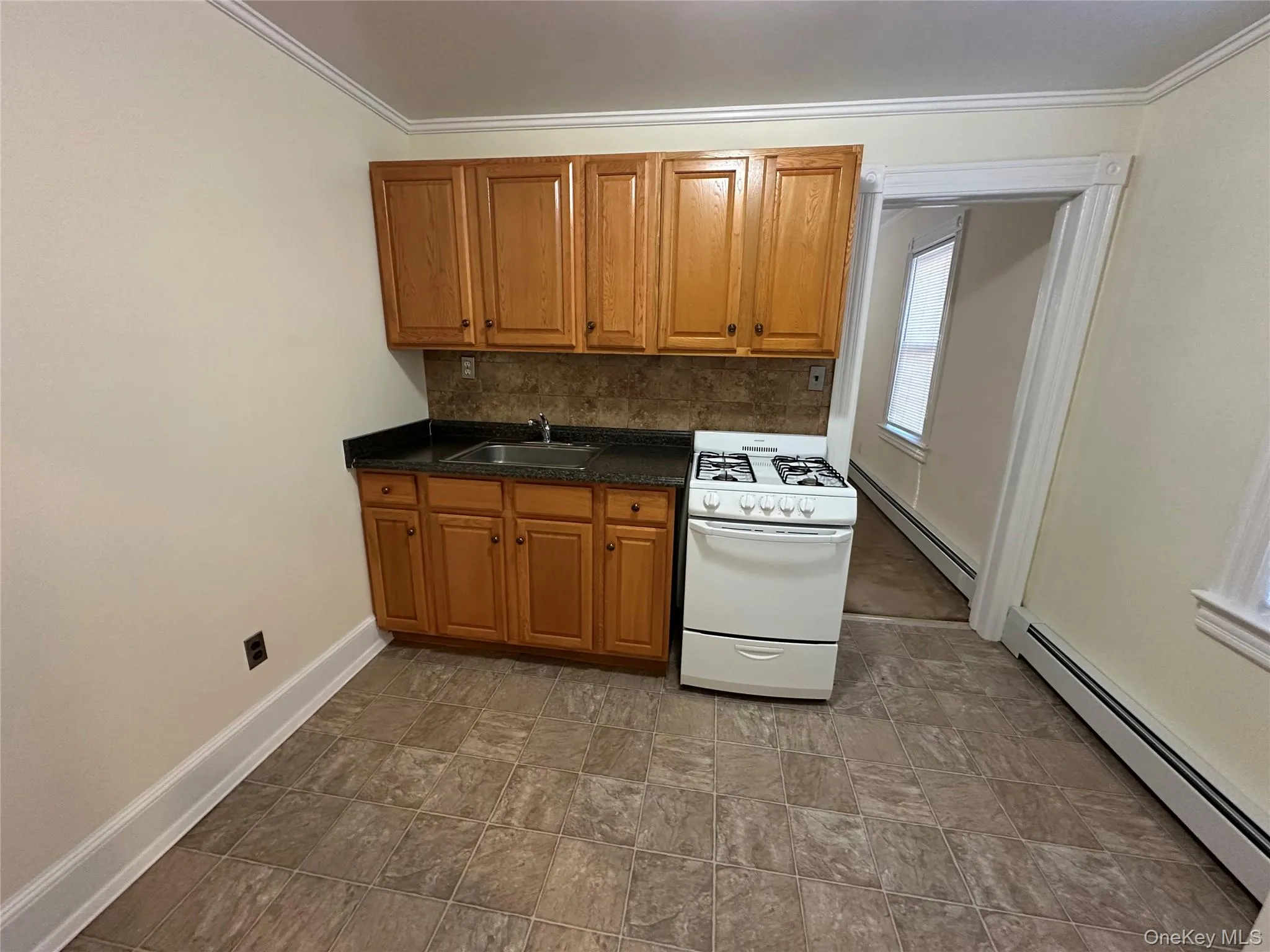 Kitchen featuring white gas stove, baseboard heating, brown cabinets, dark countertops, and ornamental molding Kitchen featuring white gas stove, baseboard heating, brown cabinets, dark countertops, and ornamental molding